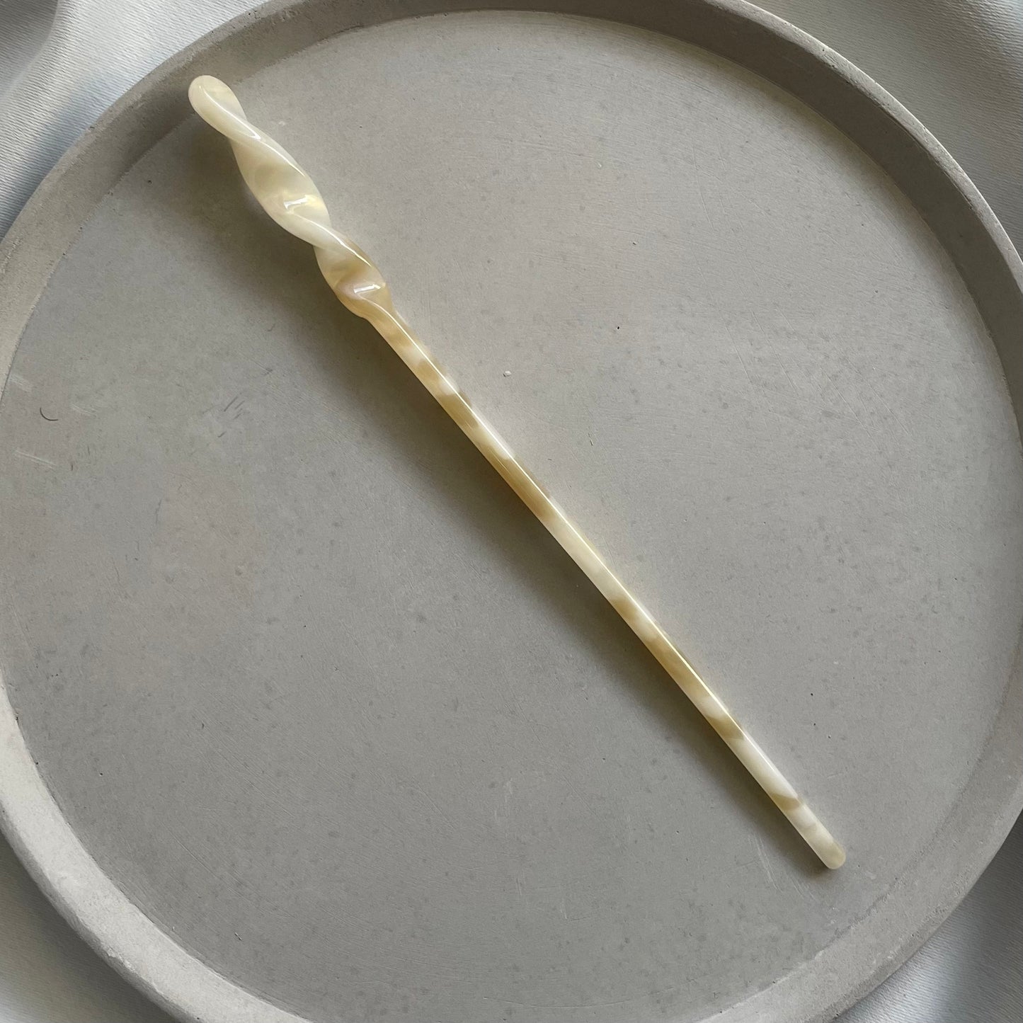 Gelber Haarstab mit weissen Details auf einer grauen Schmuckschale.
