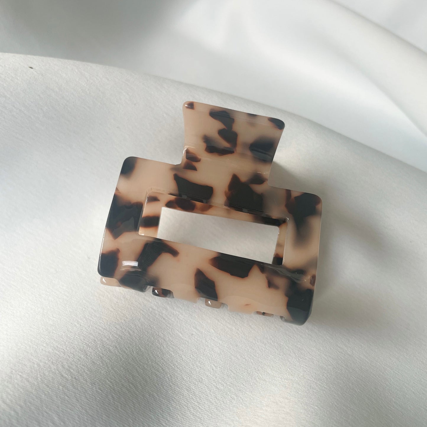 eine mittelgrosse quadratische Haarspange (5 cm) in tortoise, die auf einem seidigen weissen Tuch liegt