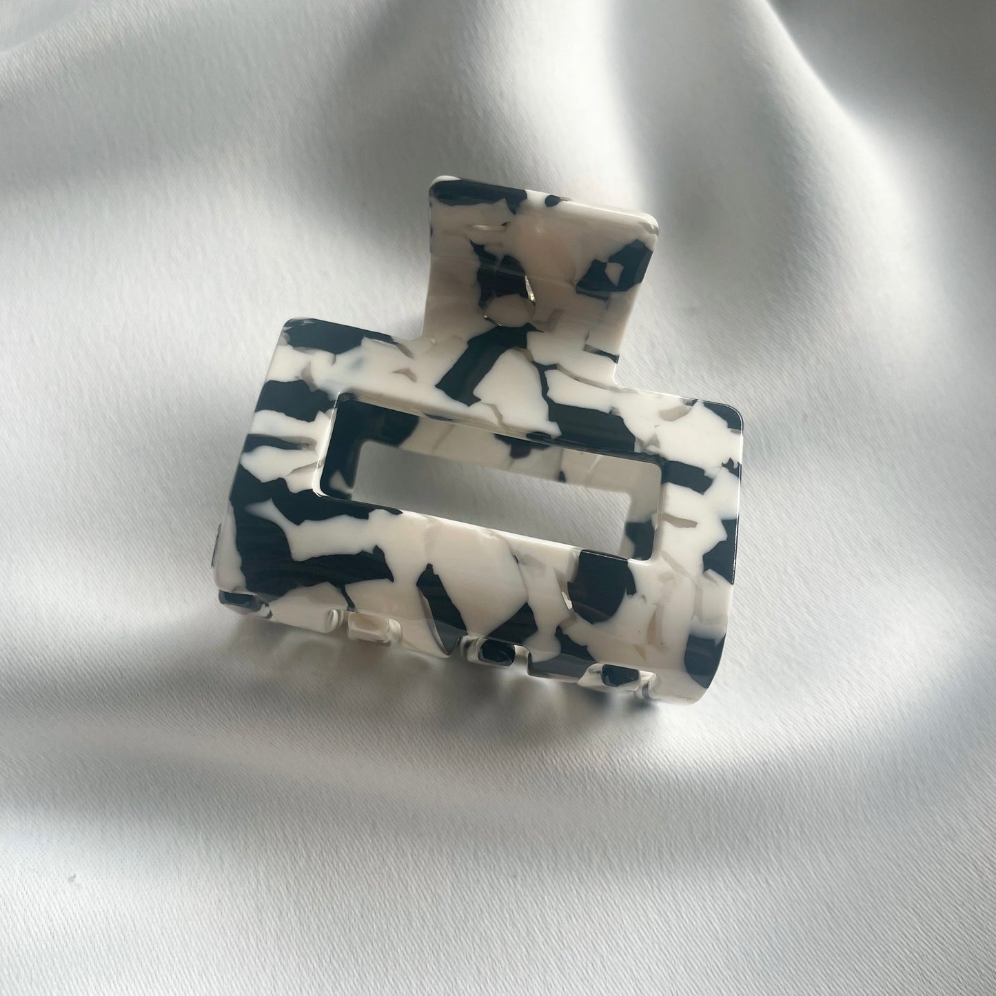 eine mittelgrosse quadratische Haarspange (5 cm) in schwarzweiss, die auf einem seidigen weissen Tuch liegt