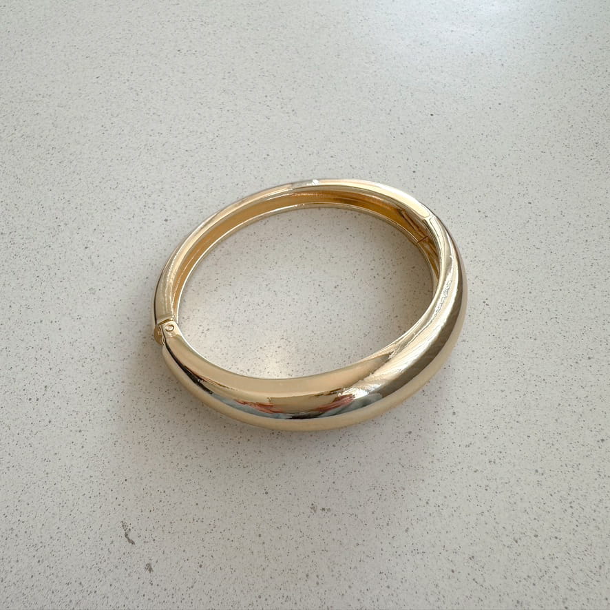 Armreifen in Gold auf neutralem Hintergrund.