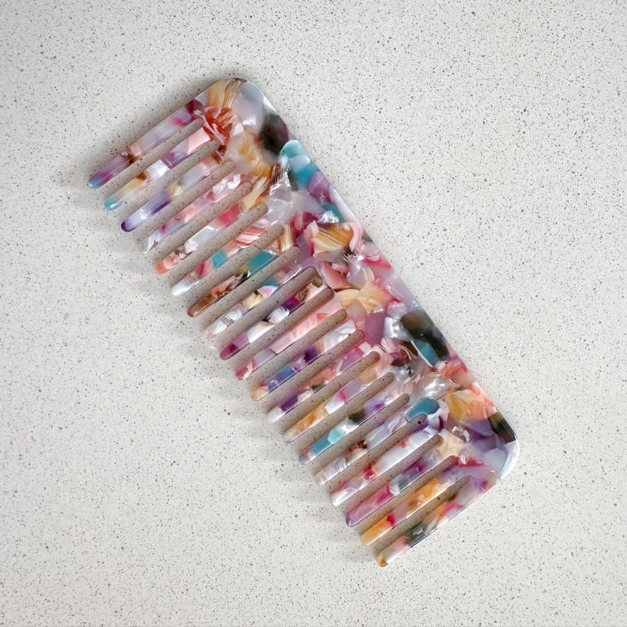 Auf dem Bild ist ein Haarkamm in bunten Farben zu sehen, der Haarkamm wird als Produktfoto auf einem neutralen Hintergrund präsentiert.