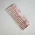 Auf dem Bild ist ein Haarkamm in rosa zu sehen, der Haarkamm wird als Produktfoto auf einem neutralen Hintergrund präsentiert.