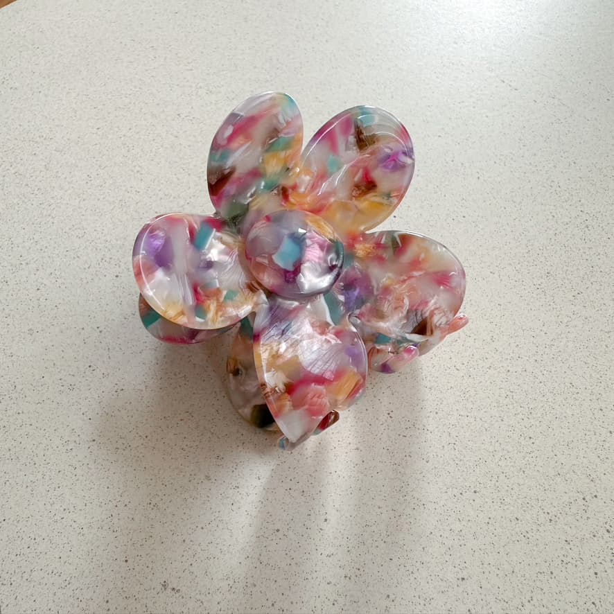 Auf dem Bild ist eine blumenförmige Haarklammer in bunt zu sehen, die Haarklammer wird als Produktfoto auf einem neutralen Hintergrund präsentiert.