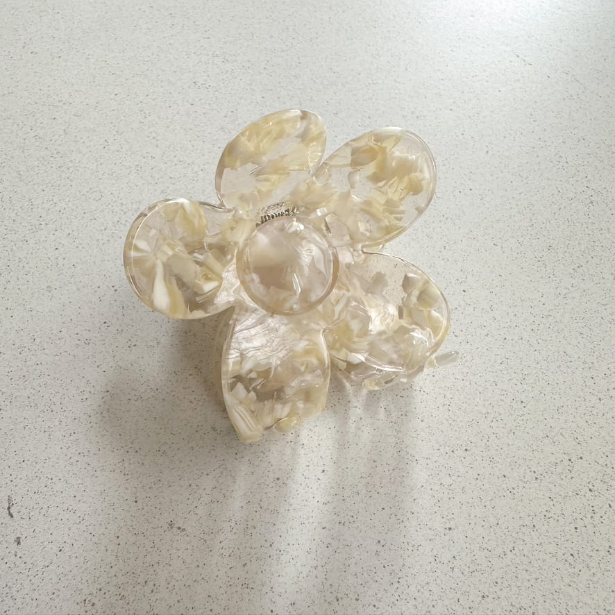 Auf dem Bild ist eine blumenförmige Haarklammer in gelb zu sehen, die Haarklammer wird als Produktfoto auf einem neutralen Hintergrund präsentiert.