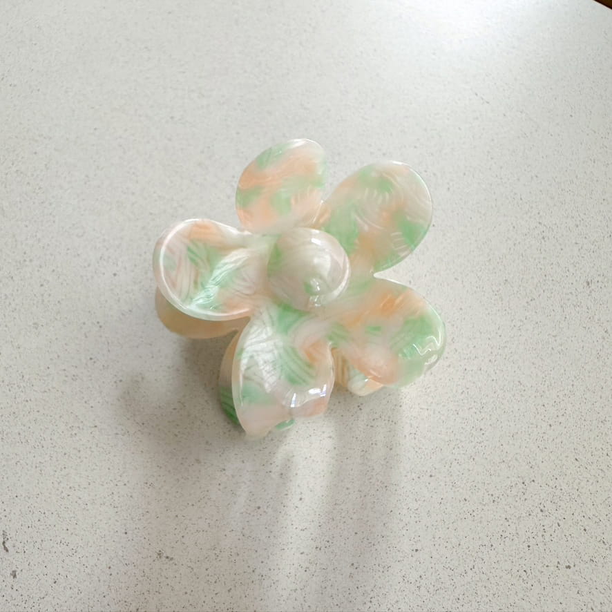 Auf dem Bild ist eine blumenförmige Haarklammer in pastell grün und orange zu sehen, die Haarklammer wird als Produktfoto auf einem neutralen Hintergrund präsentiert.