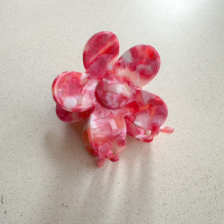 Auf dem Bild ist eine blumenförmige Haarklammer in pink zu sehen, die Haarklammer wird als Produktfoto auf einem neutralen Hintergrund präsentiert.