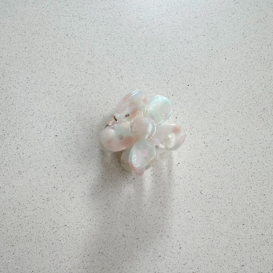 Auf dem Bild ist eine kleine blumenförmige Haarklammer in hellen Pastellfarben zu sehen, die Haarklammer wird als Produktfoto auf einem neutralen Hintergrund präsentiert.