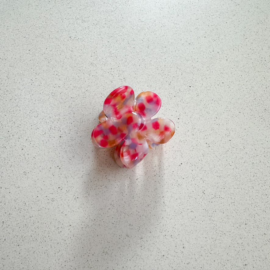 Auf dem Bild ist eine kleine blumenförmige Haarklammer in rot zu sehen, die Haarklammer wird als Produktfoto auf einem neutralen Hintergrund präsentiert.