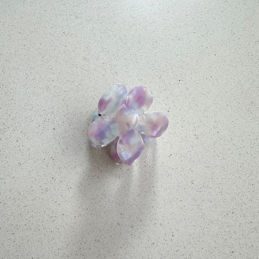 Auf dem Bild ist eine kleine blumenförmige Haarklammer in violett zu sehen, die Haarklammer wird als Produktfoto auf einem neutralen Hintergrund präsentiert.