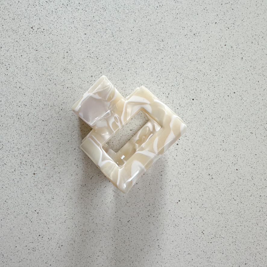 Auf dem Bild ist eine kleine quadratische Haarklammer in beige zu sehen, die Haarklammer wird als Produktfoto auf einem neutralen Hintergrund präsentiert.