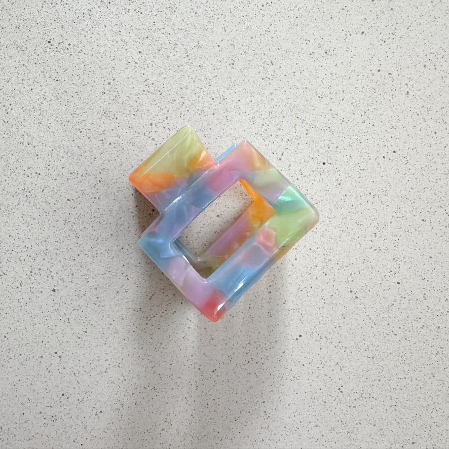 Auf dem Bild ist eine kleine quadratische Haarklammer in knalligen Farben zu sehen, die Haarklammer wird als Produktfoto auf einem neutralen Hintergrund präsentiert.