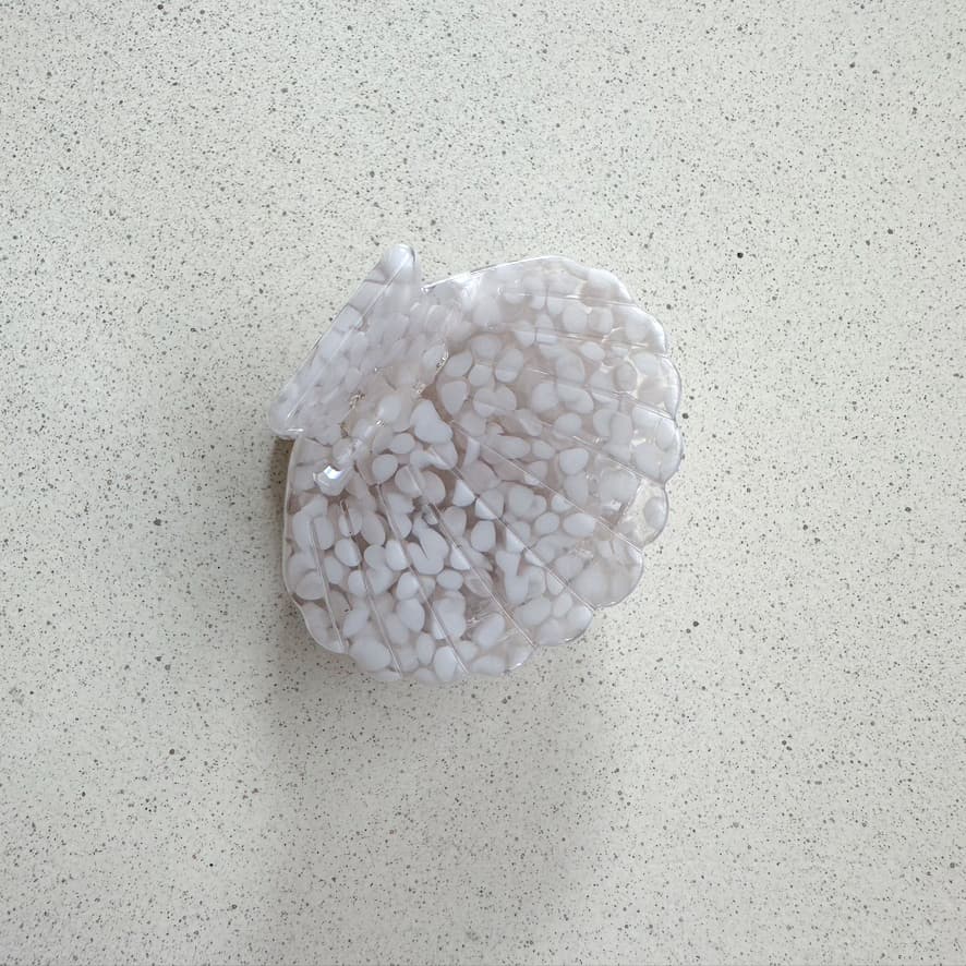 Auf dem Bild ist eine kleine muschelförmige Haarklammer in weiss zu sehen, die Haarklammer wird als Produktfoto auf einem neutralen Hintergrund präsentiert.