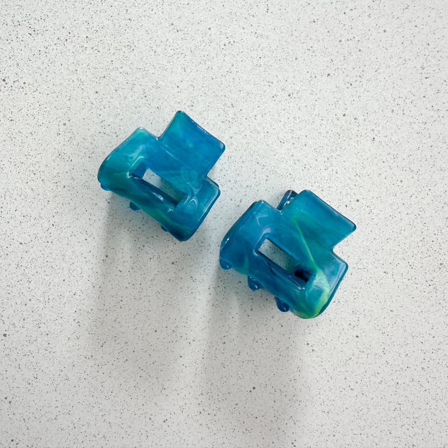 Auf dem Bild sind zwei kleine mini Haarklammer in türkis zu sehen, die Haarklammen werden als Produktfoto auf einem neutralen Hintergrund präsentiert.