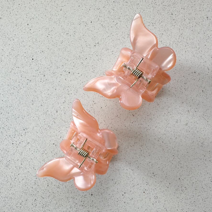 Auf dem Bild sind zwei kleine Schmetterling-Haarklammern in peach zu sehen, die Haarklammern werden als Produktfoto auf einem neutralen Hintergrund präsentiert. 
