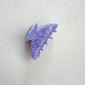 Auf dem Bild ist eine violett gepunktete Haarklammer zu sehen, die Haarklammer wird als Produktfoto auf einem neutralen Hintergrund präsentiert.