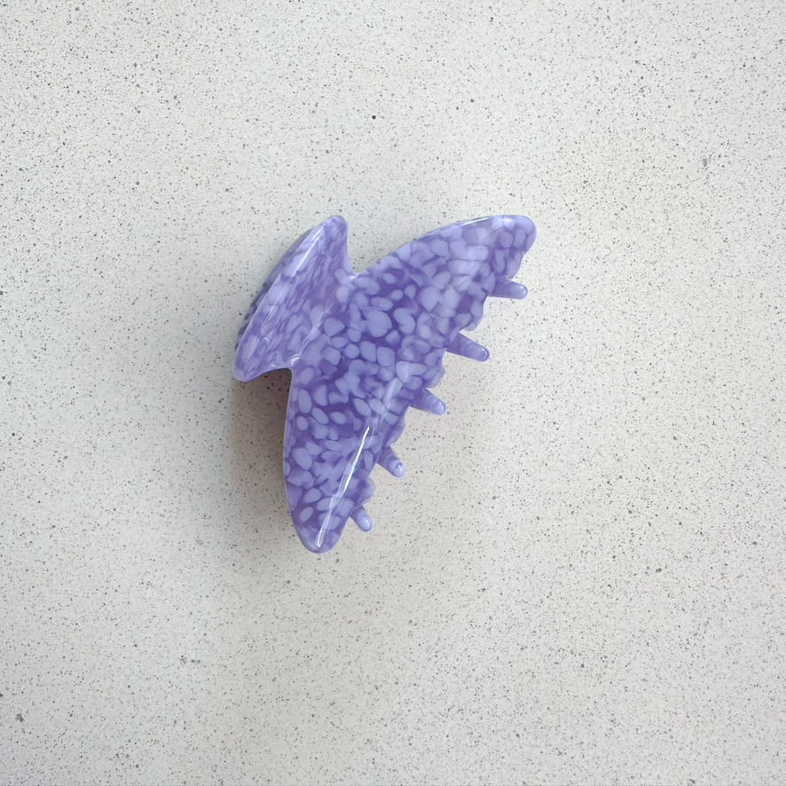 Auf dem Bild ist eine violett gepunktete Haarklammer zu sehen, die Haarklammer wird als Produktfoto auf einem neutralen Hintergrund präsentiert.