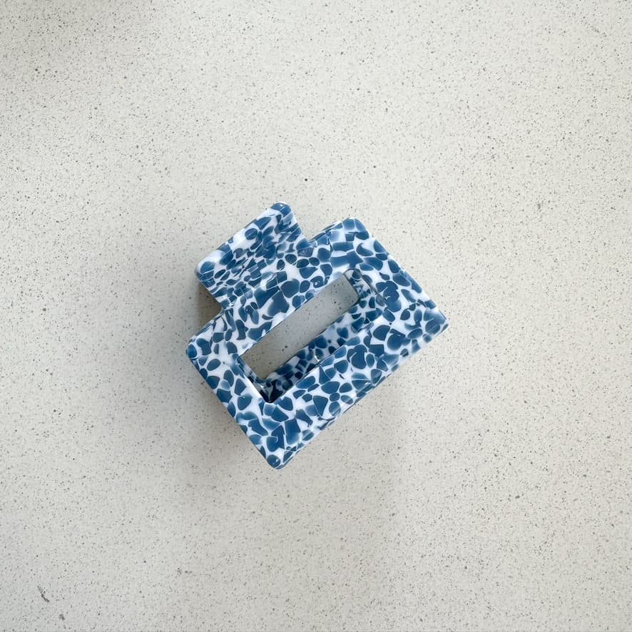 Auf dem Bild ist eine quadratische Haarklammer in blau zu sehen, die Haarklammer wird als Produktfoto auf einem neutralen Hintergrund präsentiert.