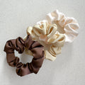 Auf dem Bild sind drei Scrunchies in braun, beige & weiss zu sehen, die Scrunchies werden als Produktfoto auf einem neutralen Hintergrund präsentiert.