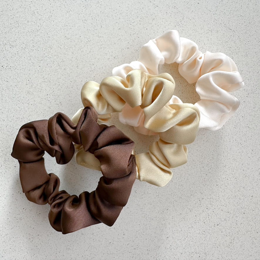 Auf dem Bild sind drei Scrunchies in braun, beige & weiss zu sehen, die Scrunchies werden als Produktfoto auf einem neutralen Hintergrund präsentiert.