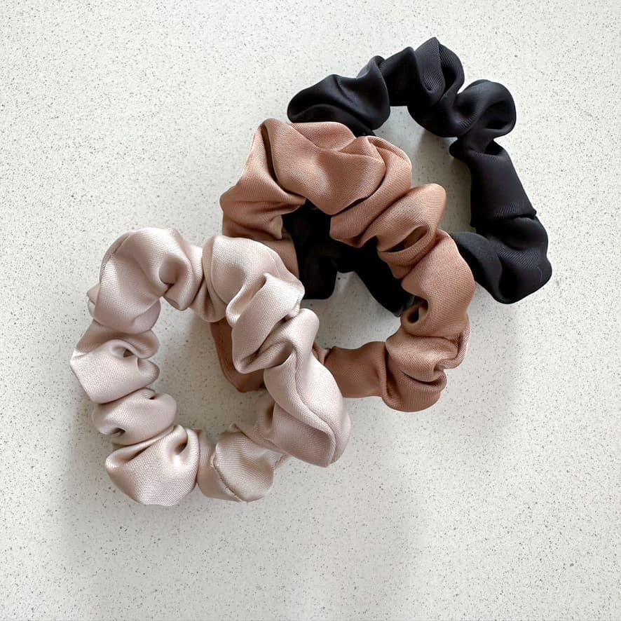 Auf dem Bild sind drei Scrunchies in hellbraun, beige & schwarz zu sehen, die Scrunchies werden als Produktfoto auf einem neutralen Hintergrund präsentiert.