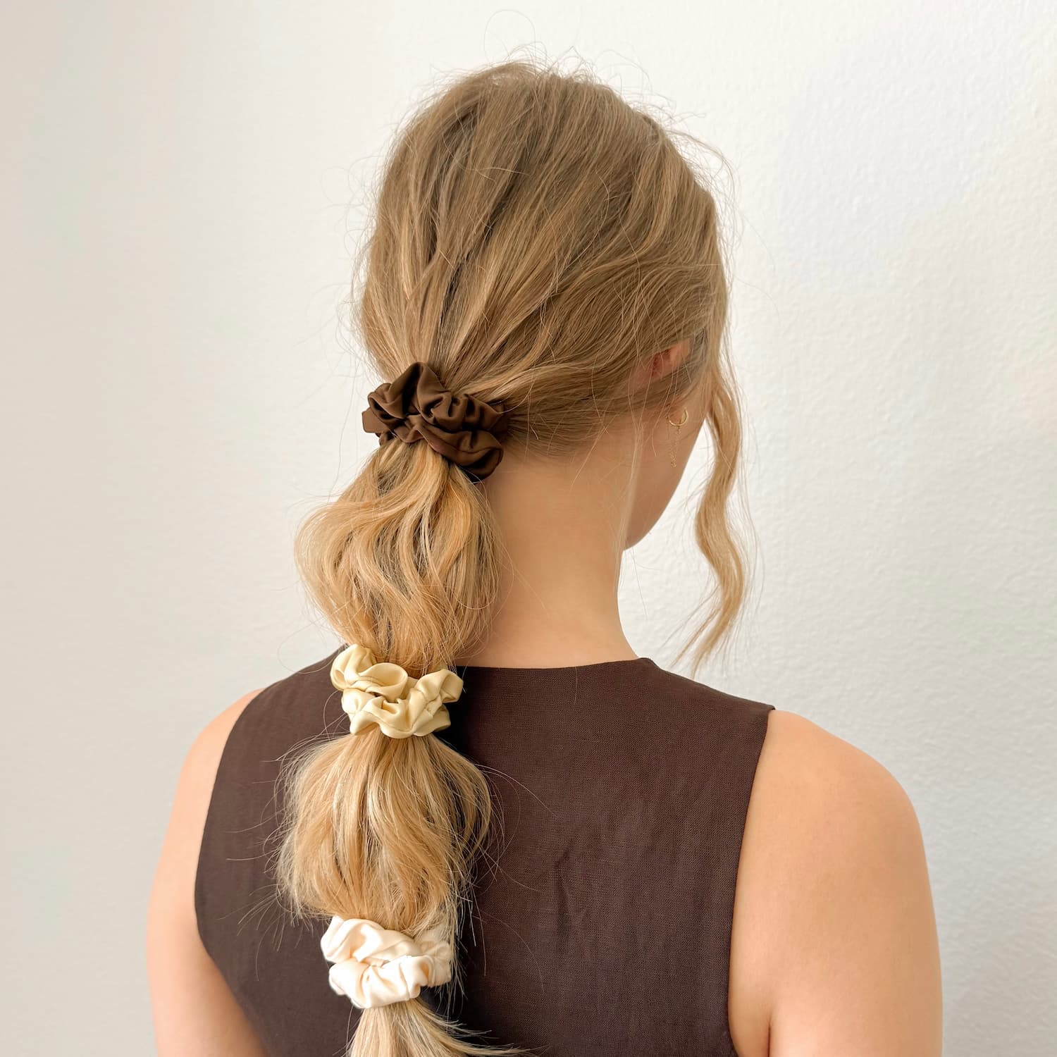 Auf dem Bild sind drei Scrunchies in braun, beige & weiss zu sehen, die Scrunchies werden getragen präsentiert.