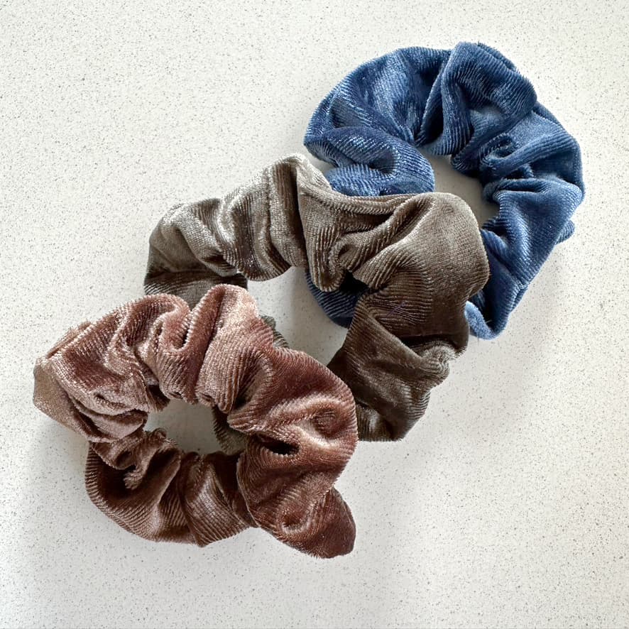 Auf dem Bild sind drei Scrunchies in blau, grün, dunkelbraun zu sehen, die Scrunchies werden als Produktfoto auf einem neutralen Hintergrund präsentiert.