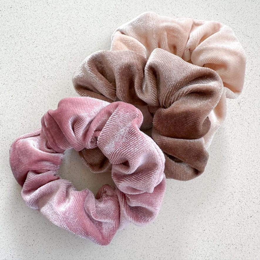 Auf dem Bild sind drei Scrunchies in rosa, hellbraun & beige zu sehen, die Scrunchies werden als Produktfoto auf einem neutralen Hintergrund präsentiert.