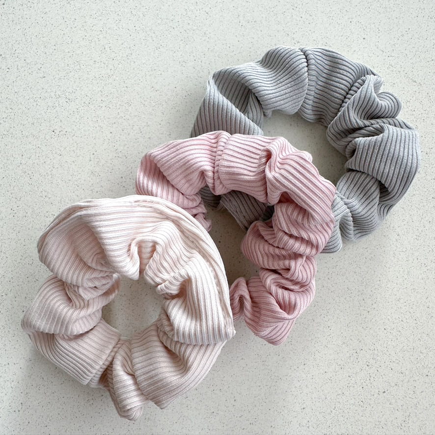 Auf dem Bild sind drei gerillte Scrunchies in frühlingshaften Farben zu sehen, die Scrunchies werden als Produktfoto auf einem neutralen Hintergrund präsentiert.