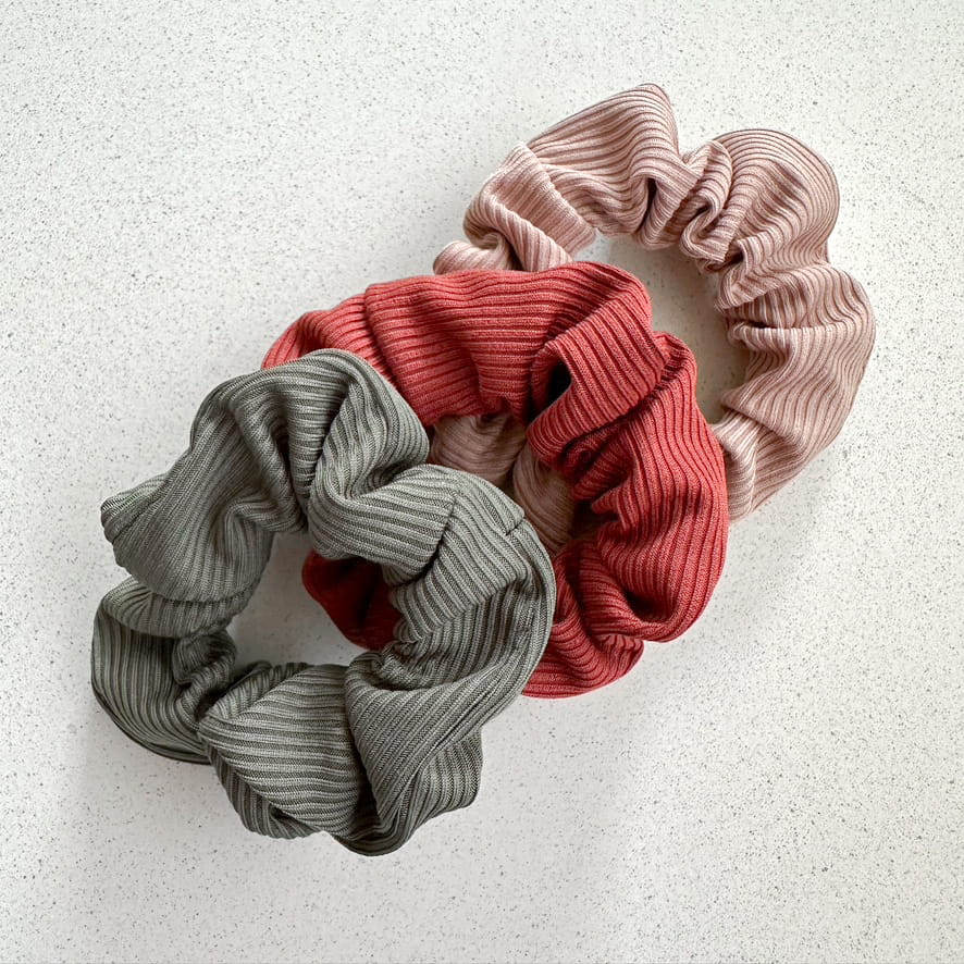 Auf dem Bild sind drei gerillte Scrunchies in herbstlichen Farben zu sehen, die Scrunchies werden als Produktfoto auf einem neutralen Hintergrund präsentiert.