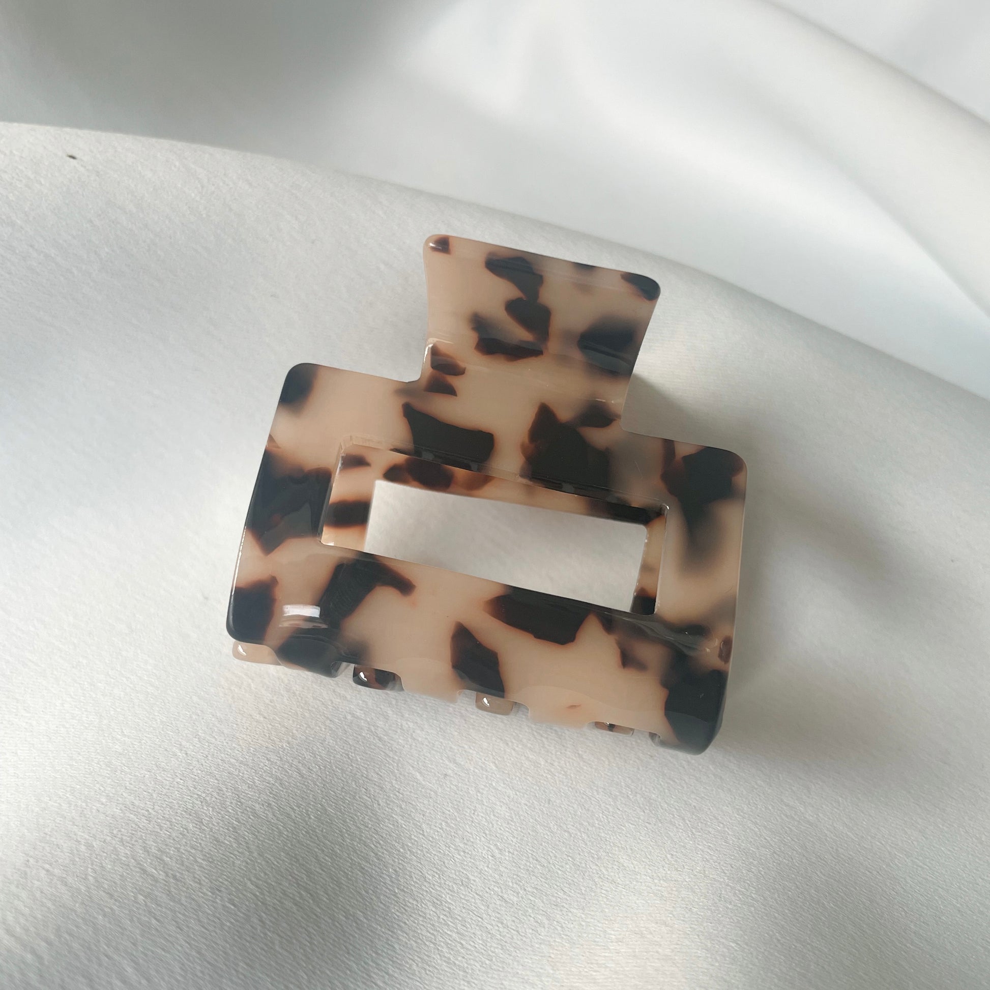 eine mittelgrosse quadratische Haarspange (5 cm) in tortoise, die auf einem seidigen weissen Tuch liegt