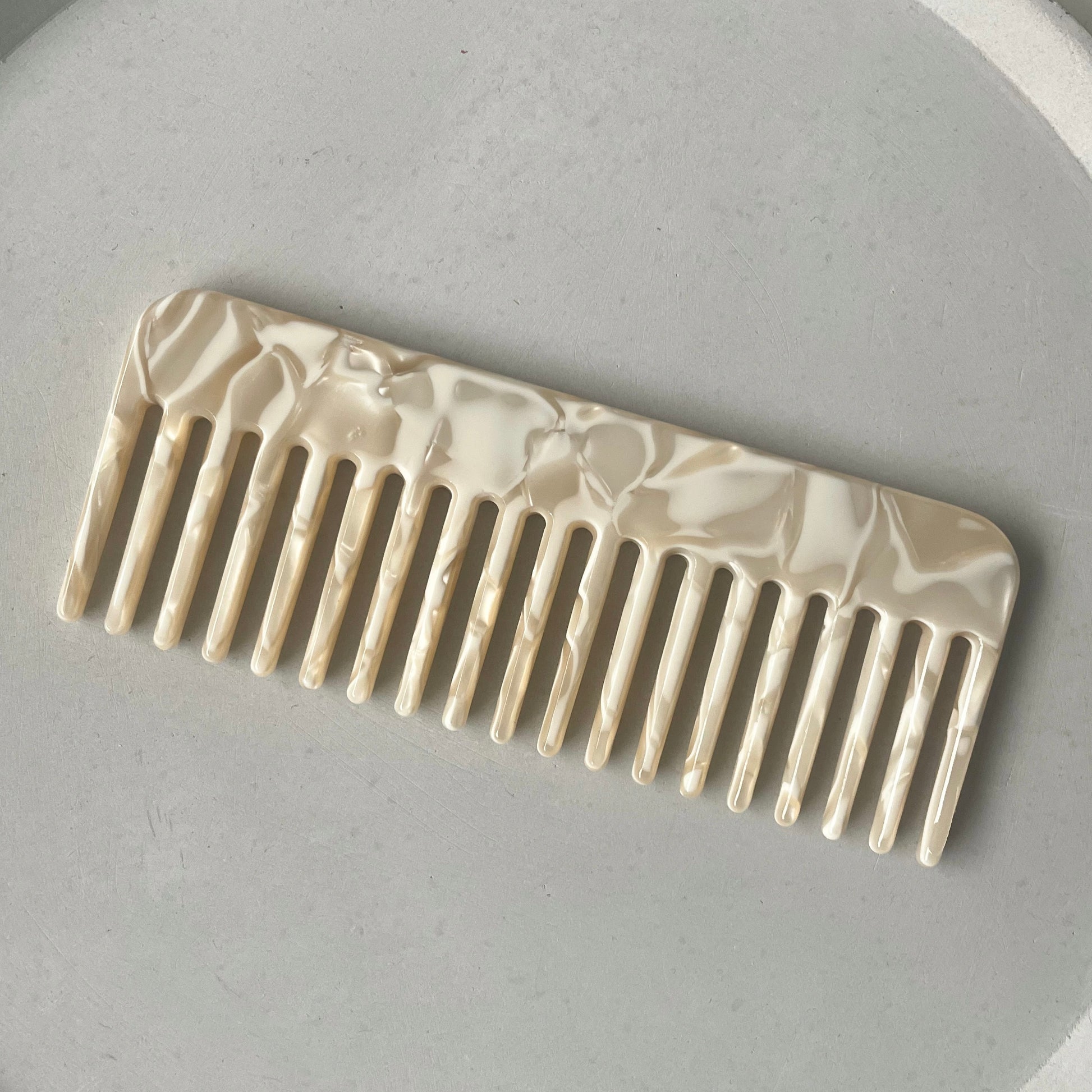 Haarkamm in beige mit weissen Details auf einem grauen Hintergrund